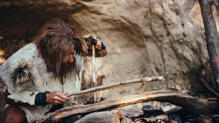 Primeval Caveman Wearing Animal Skin Trying to make a Fire with Bow Drill Method. Neanderthal...