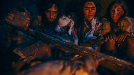 Neanderthal or Homo Sapiens Family Cooking Animal Meat over Bonfire and then Eating it. Tribe of...