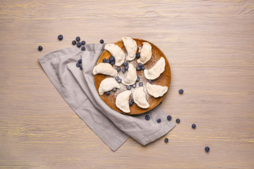 Plate with raw dumplings and blueberries on wooden background