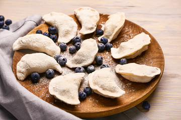 Plate with raw dumplings and blueberries on wooden background