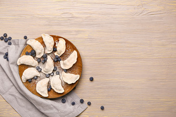Plate with raw dumplings and blueberries on wooden background