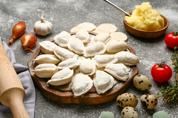 Board with raw dumplings and ingredients on grey background