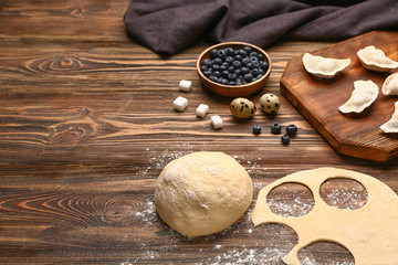 Raw dough and dumplings with ingredients on wooden background