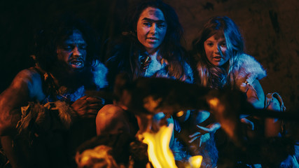Fototapeta na wymiar Neanderthal or Homo Sapiens Family Cooking Animal Meat over Bonfire and then Eating it. Tribe of Prehistoric Hunter-Gatherers Wearing Animal Skins Grilling and Eating Meat in Cave at Night