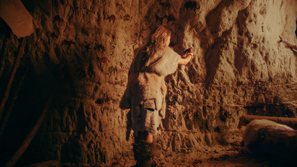 Back View of a Primitive Prehistoric Neanderthal Child Wearing Animal Skin Draws Animals and...