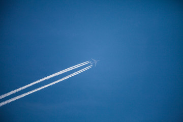 Jumbo Jet in dizzy height with two white condensation trails in the blue sky