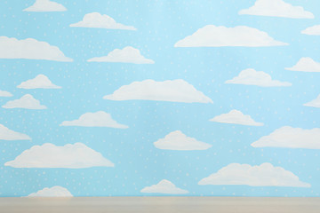 Wooden table near wall with painted blue sky. Idea for baby room interior