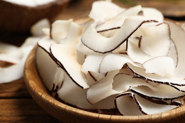 Tasty coconut chips in wooden plate, closeup