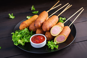 Traditional American corn dogs with mustard and ketchup on black plate. Street food. Copy space