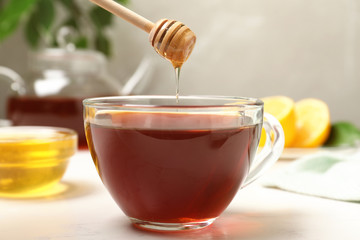 Honey dripping into cup of tea on white table