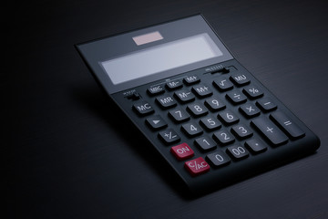 Side view of a black accounting calculator with a blank display on a dark wooden table with copy space for text. Calculation of taxes, payments and profits concept