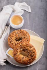 fresh bagels with butter and cheese on plate and cup of coffee on ceramic background