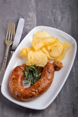 typical portuguese smoked sausage alheira with potato chips on white dish