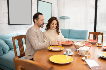 Happy couple sitting at the table with noce ckockery in a light room