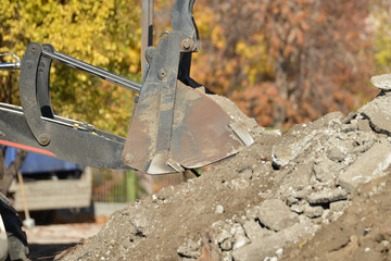 A tractor with a bucket performs construction work on cleaning the territory at a construction site.