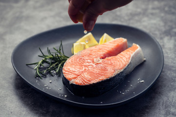 raw salmon with rosemary and lemon on dark plate