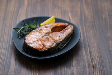 fried salmon with lemon and rosemary on dark dish on ceramic background