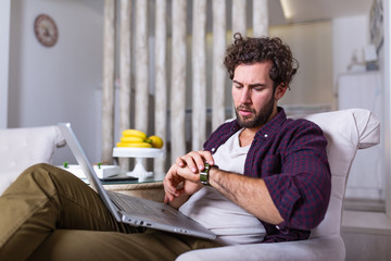 Freelancer man working from home and checking time on his wrist watch.