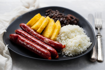 sausages with rice, black beans, and pineapple on dark dish