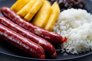 sausages with rice, black beans, and pineapple on dark dish