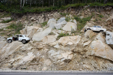 Old rusty cars stuck on the steep mighty Rocky mountains of the Altai territory, covered with forest. The background is light brown.