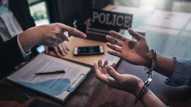 Police officer interrogating suspect or criminal man with handcuffs arrested at the investigation.