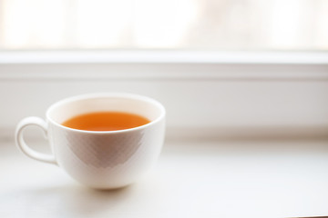 white cup with tea stands on the windowsill on the window