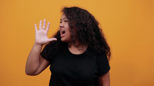 Young woman with overweight showing palm at camera, screaming over isolated orange background wearing fashion black shirt. People lifestyle concept.