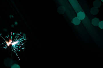 Sparkler in turquoise and white light on a black background.
