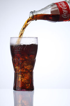 pouring coca cola to coca cola glass with ice cube