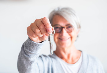 one senior and mature woman holding a key of a house or car - seller her property to someone ready...