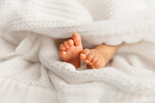 Adorable infant feet covered in a white blanket, maternity and babyhood concept