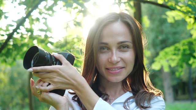 Close-up woman photographs model through the rays at sunset.Pretty smiling woman photographer is making photos with professional camera in a park on a soft background of green foliage and spraying