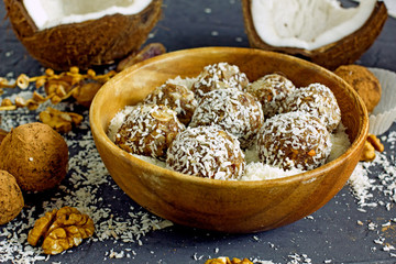 Raw food balls.Handmade vegan sweets made from almonds, walnuts, dates, raisins, coconut and cocoa. Raw food candies in coconut and cocoa close-up on white paper on a dark table laid out in rows. 