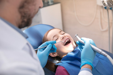 Young caucasian girl calm and happy visiting dentist's office for prevention and treatment of the oral cavity. Child and doctor while checkup teeth. Healthy lifestyle, healthcare and medicine concept.