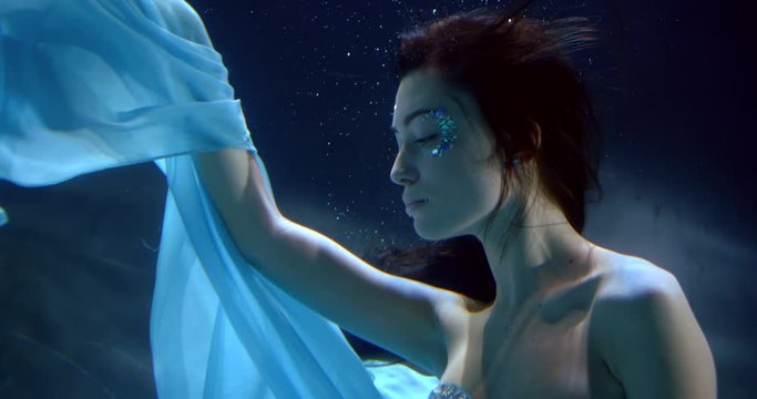 fantastic oceanic nymph is floating in water in darkness in blue lights