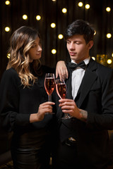 Elegant couple toasting the New Year with champagne and joy as they clink glasses against strings of twinkling party lights