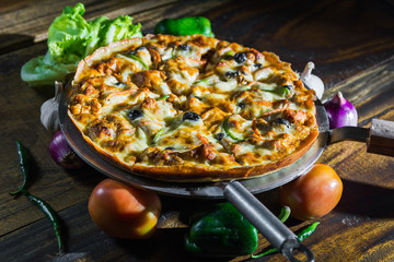 Chicken Pizza with rich cheese tomato onion garlic fresh green chili and cabbage on a wooden table dramatic light