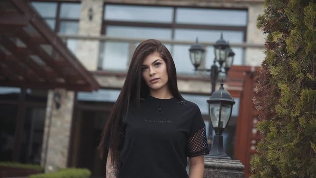 Portrait of attractive brunette stands in pose near house at camera