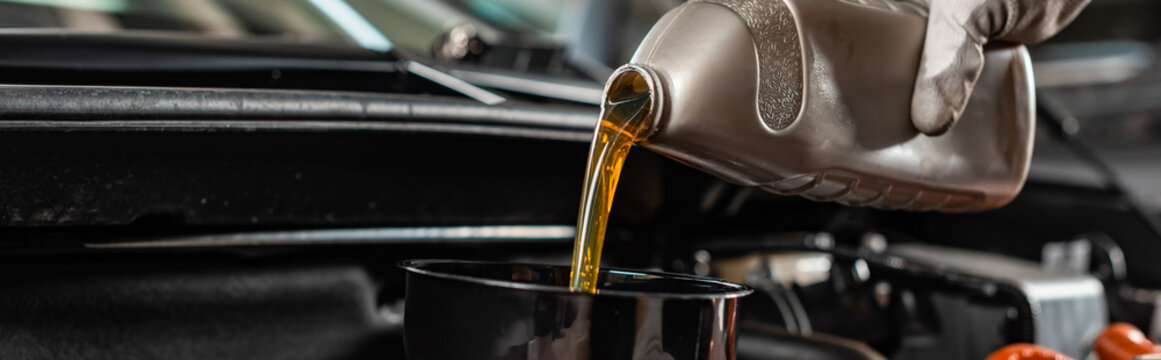 partial view of mechanic pouring machine oil at car engine, panoramic shot
