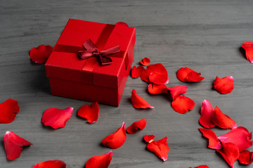 Beautiful red roses next to a gift red box on a dark cement background.