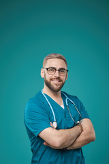 Waist up studio portrait of confident handsome doctor standing against blue turquoise background...