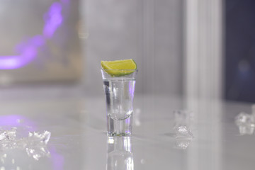glasses of silver tequila, a slice of lime and pieces of ice on the table