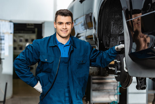 smiling mechanic looking at camera while touching disc brakes of car