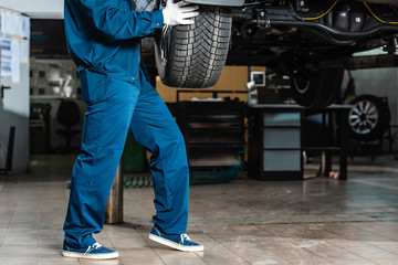 cropped view of mechanic installing wheel on raised car in workshop