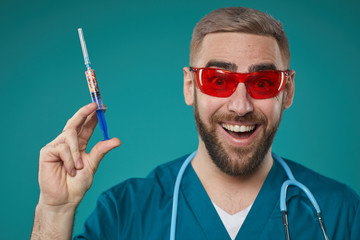 Humorous head and shoulders studio portrait shot of enthusiastic doctor in eyewear holding injector looking at camera smiling