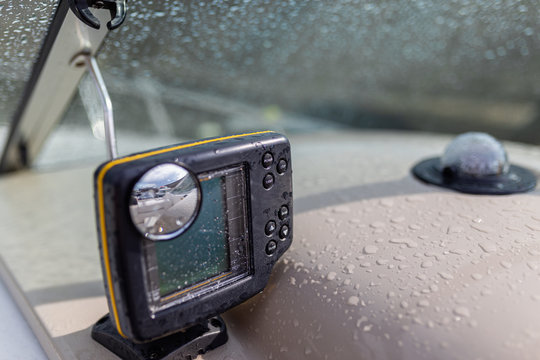 Gps Navigation System In Raindrops For Swimming In The Sea Located On The Dashboard Of A Pleasure Yacht. Close-up Black Modern Chartplotter Device On Motor Boat Dashboard, Local Time, Depth, Map, Trip