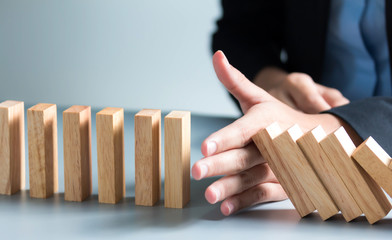 Close up of businessman hand Stopping Falling wooden Dominoes effect from continuous toppled or...