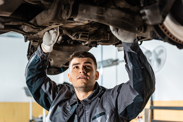 attentive mechanic examining raised car in workshop