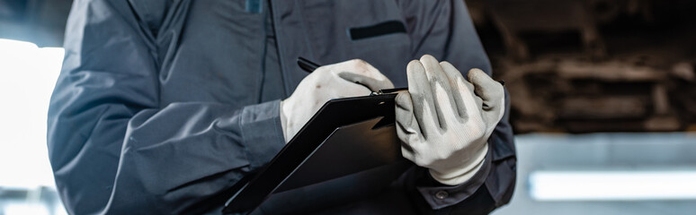 cropped view of mechanic writing on clipboard, panoramic shot